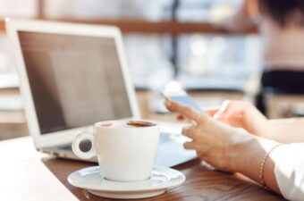 close-up shot of woman working on laptop and smartphone inside a coffee shop