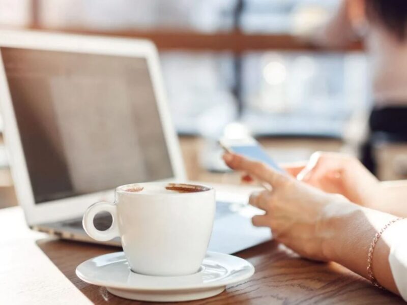 close-up shot of woman working on laptop and smartphone inside a coffee shop